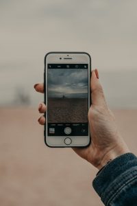 anonymous female tourist photographing seascape on sandy coast